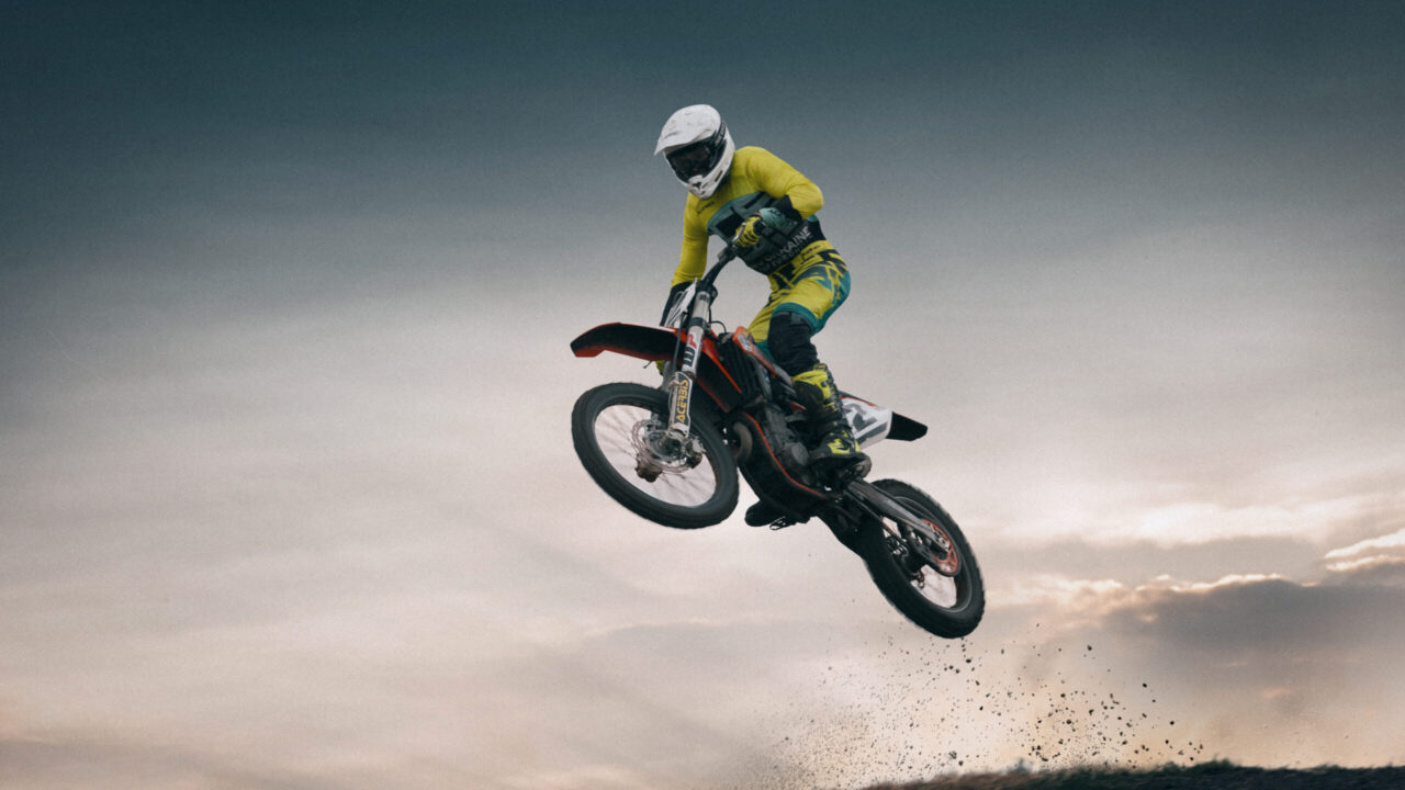 Pilote de motocross en position de base, debout sur les repose-pieds, buste avancé, coudes hauts