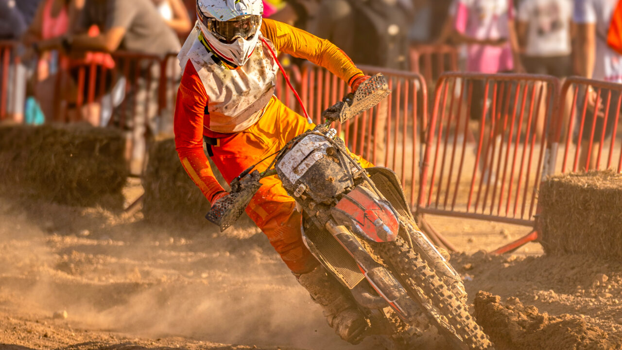 Pilote de motocross en position de virage, buste avancé et jambe intérieure ouverte, roue arrière dérapant dans la poussière