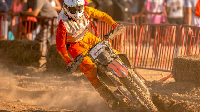 Pilote de motocross en position de virage, buste avancé et jambe intérieure ouverte, roue arrière dérapant dans la poussière