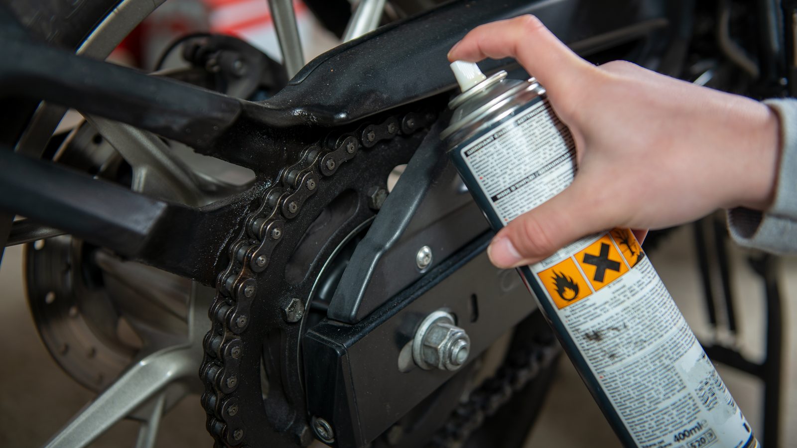 Application d'un spray de graisse sur la chaîne d'une moto, roue arrière