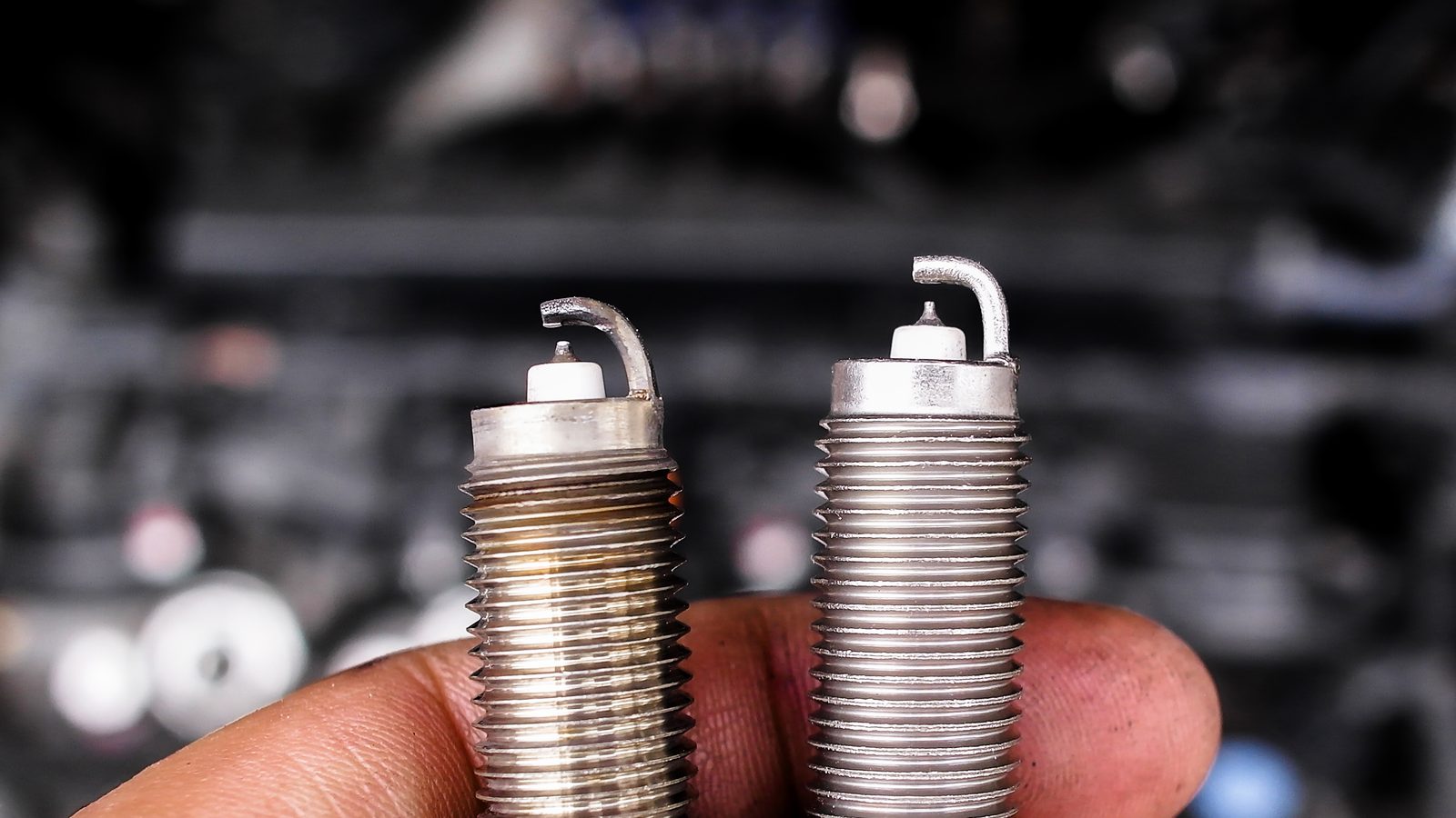 Bougie usagée et bougie neuve tenues côte à côte pour comparer l'électrode