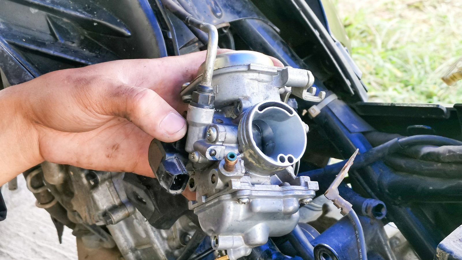 Carburateur de moto déposé et tenu en main au-dessus d'un plan de travail