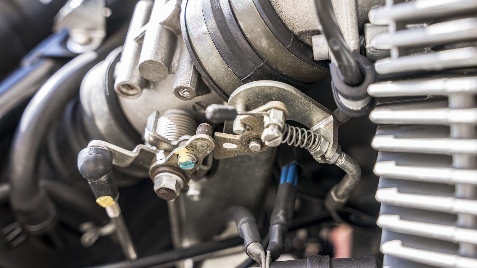 Carburateur de moto monté sur le moteur, durites d'essence et câbles de commande visibles