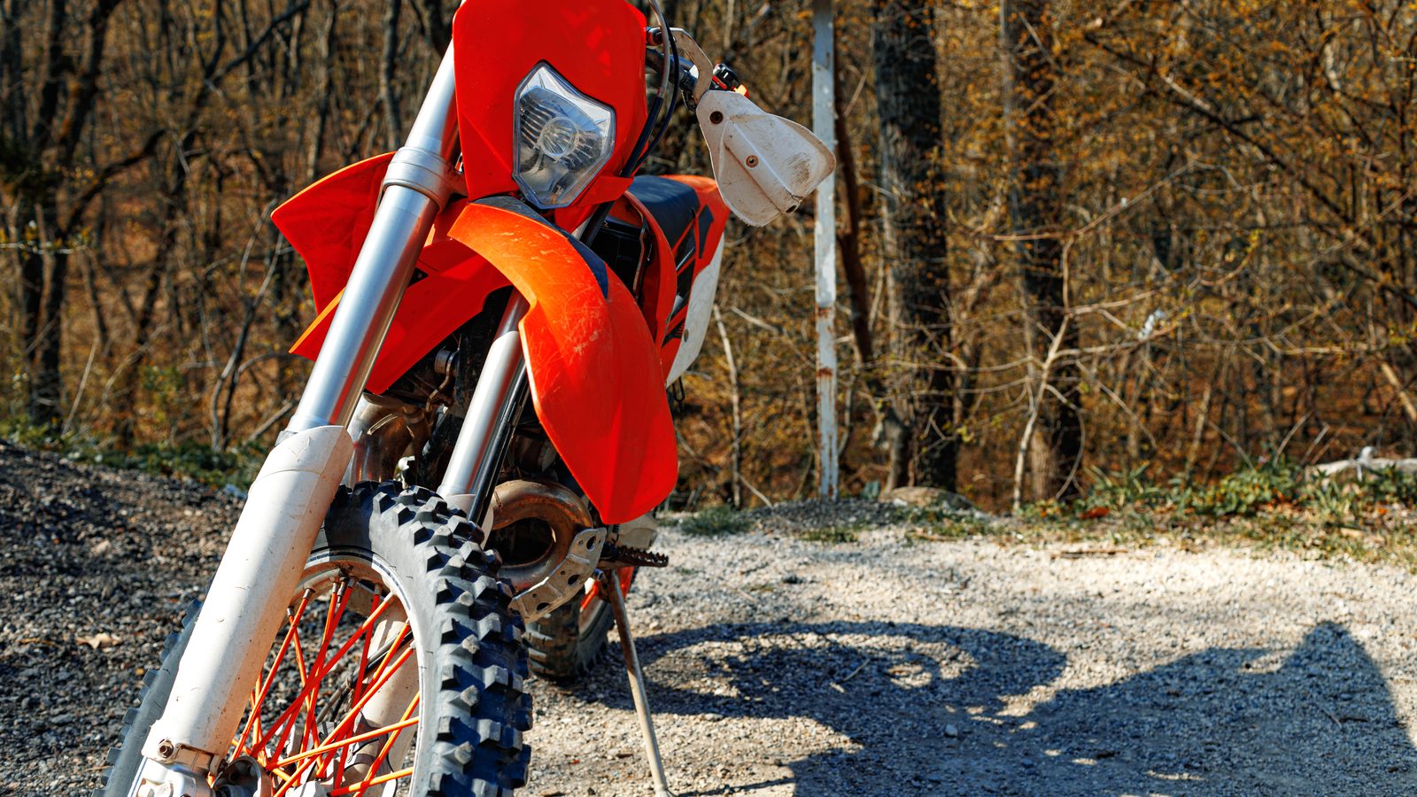 Détail d'une roue de moto de cross posée sur un sol de terre et de graviers