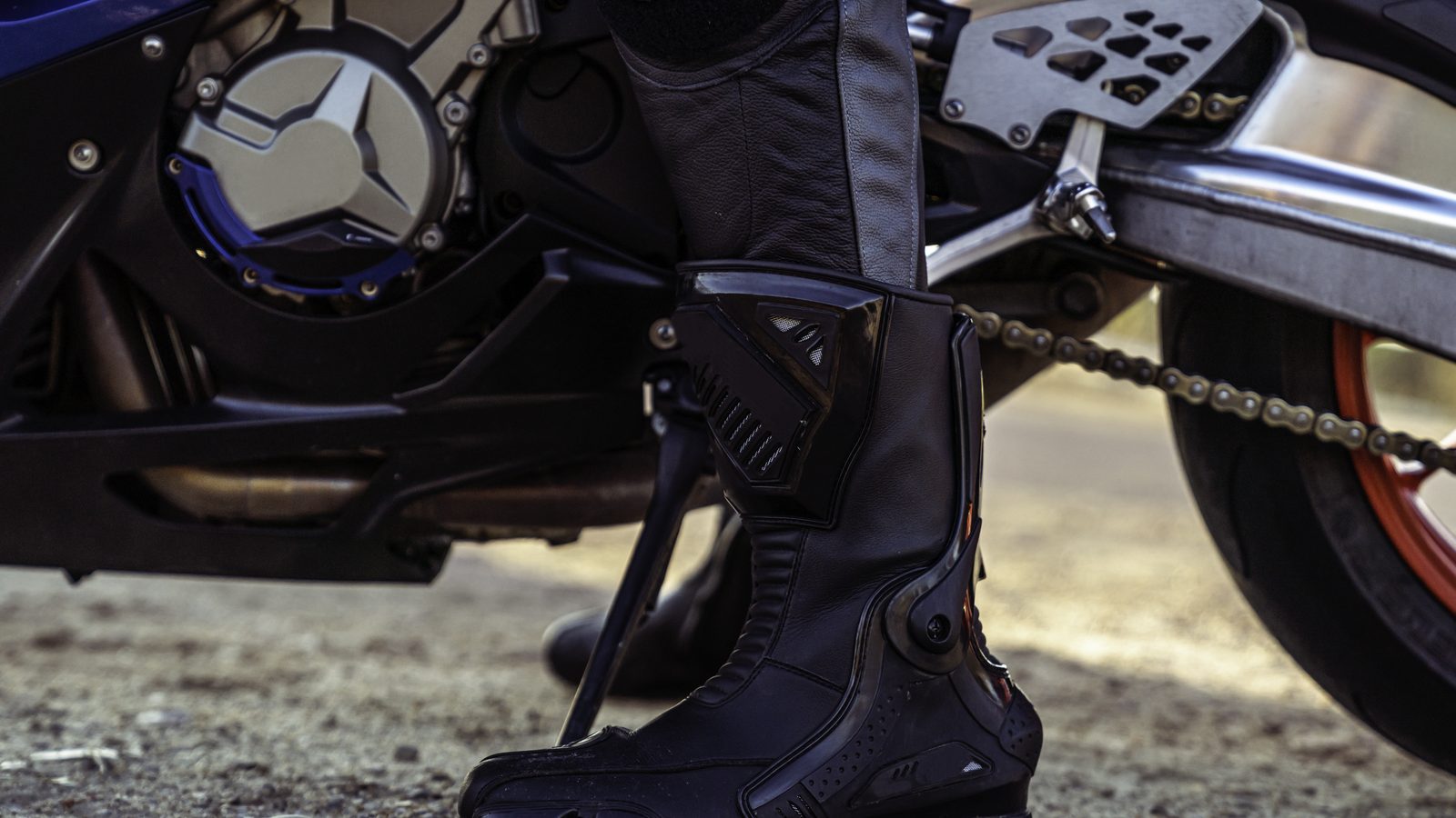 Gros plan sur la botte d'un pilote posée au sol devant la roue de sa moto