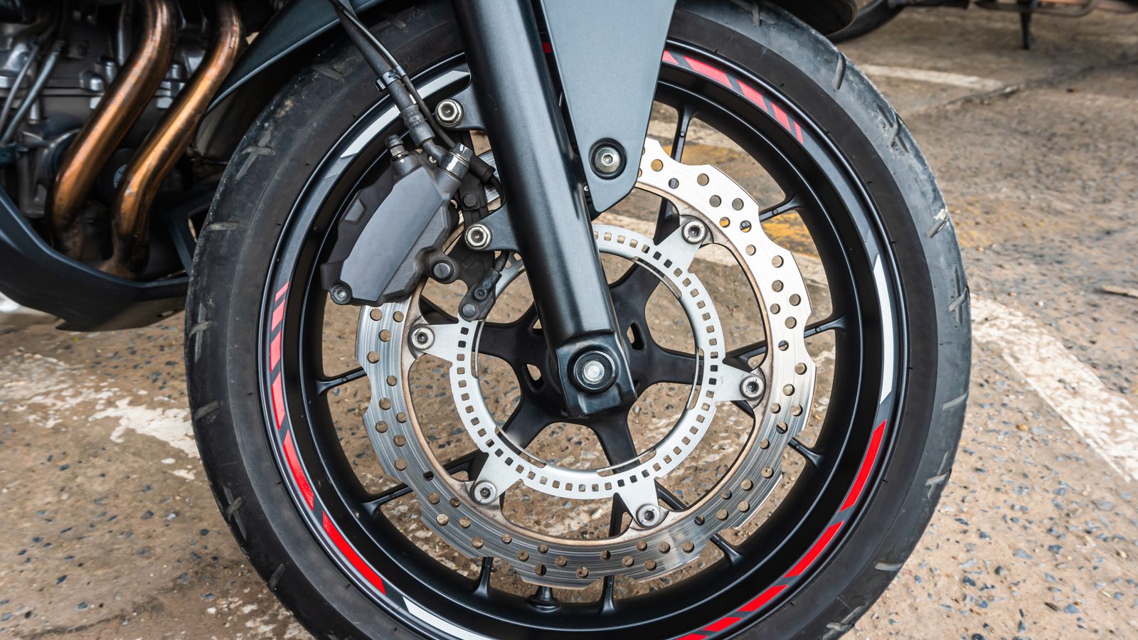 Gros plan sur le disque et l'étrier de frein avant d'une moto, roue vue de trois quarts