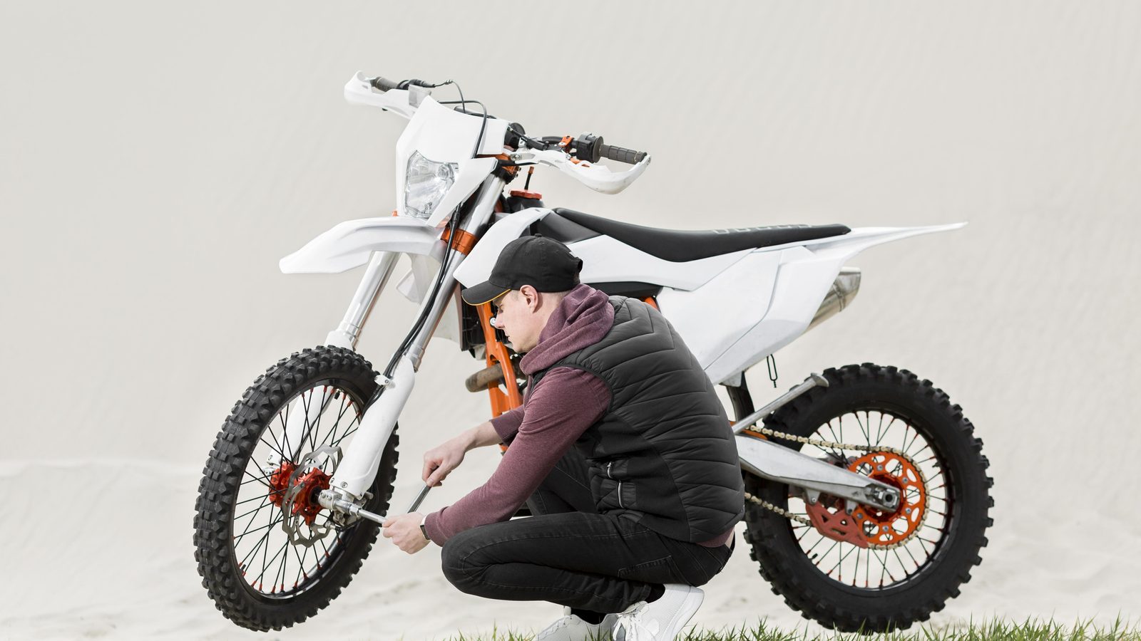 Homme agenouillé près de sa moto tout-terrain vérifiant les fixations en extérieur