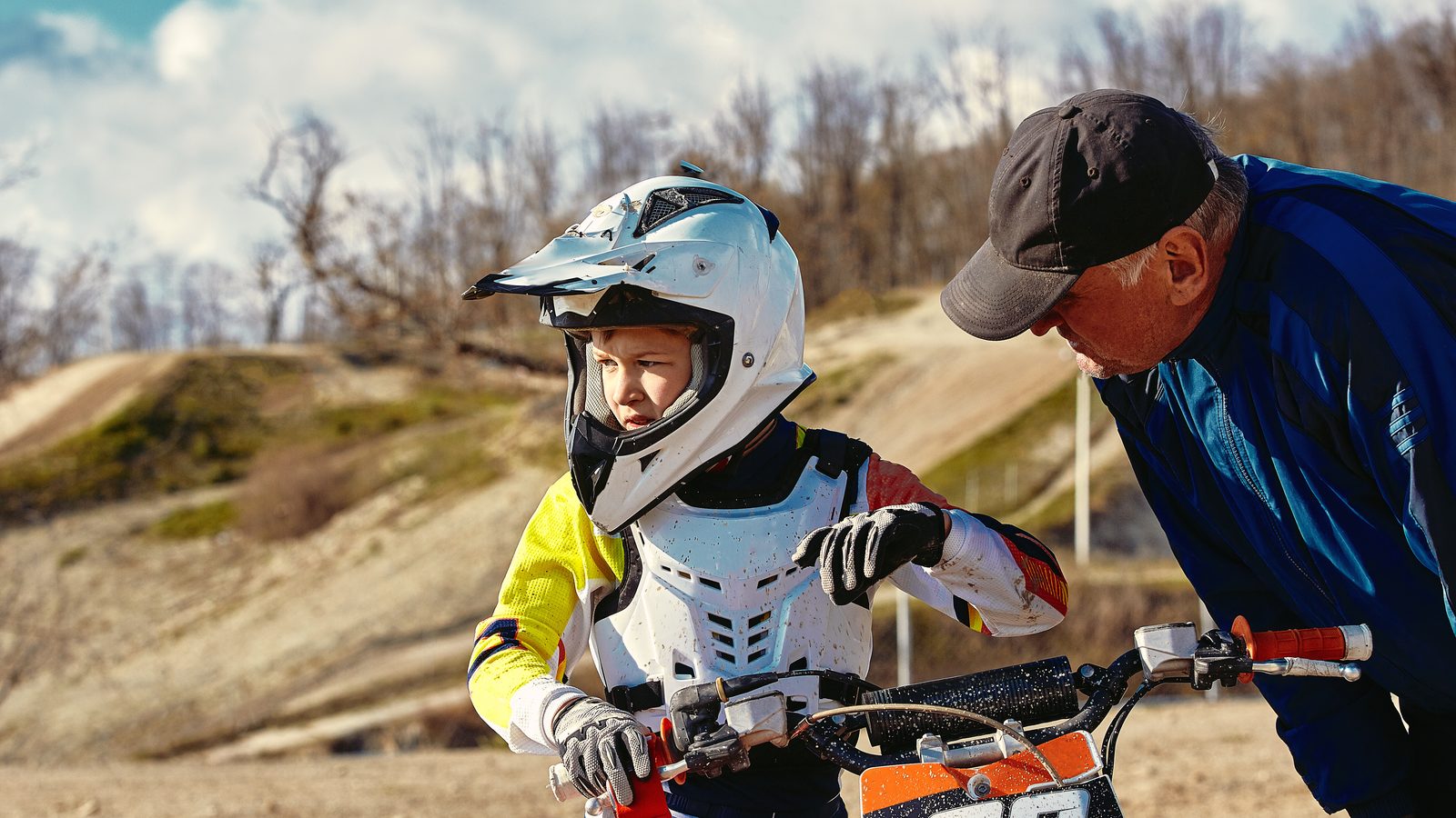 Jeune pilote sur sa moto lors d'une épreuve junior, son coach debout à côté de lui