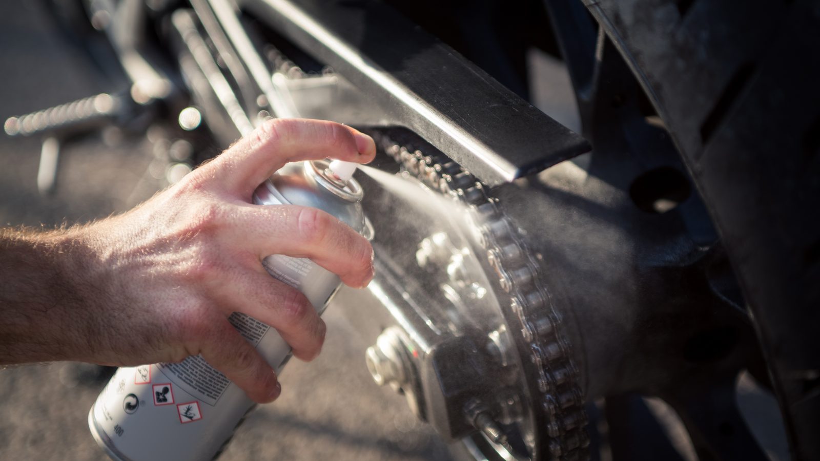 Main appliquant un spray lubrifiant sur la chaîne d'une moto après lavage