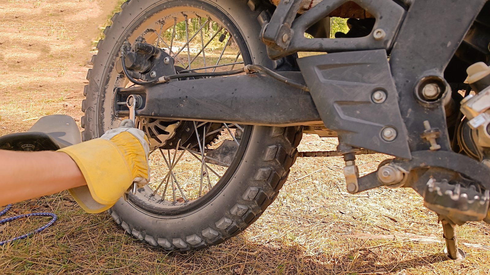 Main gantée serrant à la clé un boulon sur la roue arrière d'une moto sale