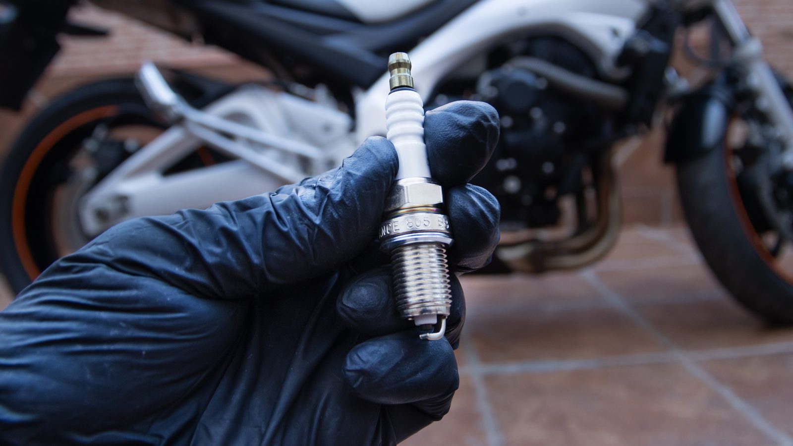 Main gantée tenant une bougie de moto tout-terrain devant le moteur en atelier