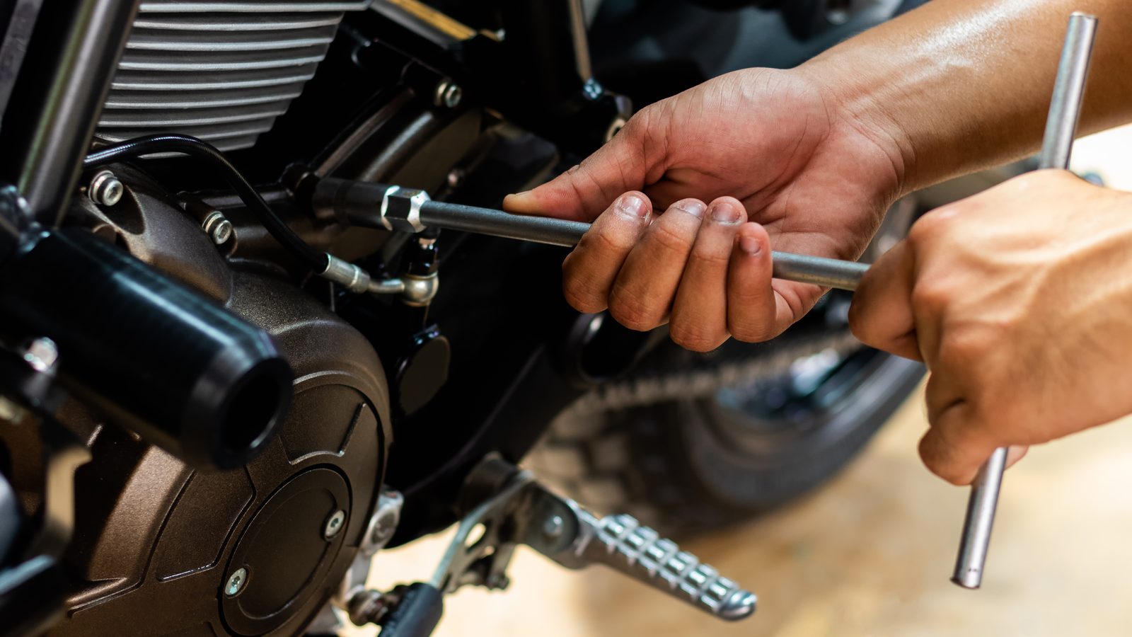 Mains d'un mécanicien avec clé et tournevis intervenant sur une moto à l'atelier