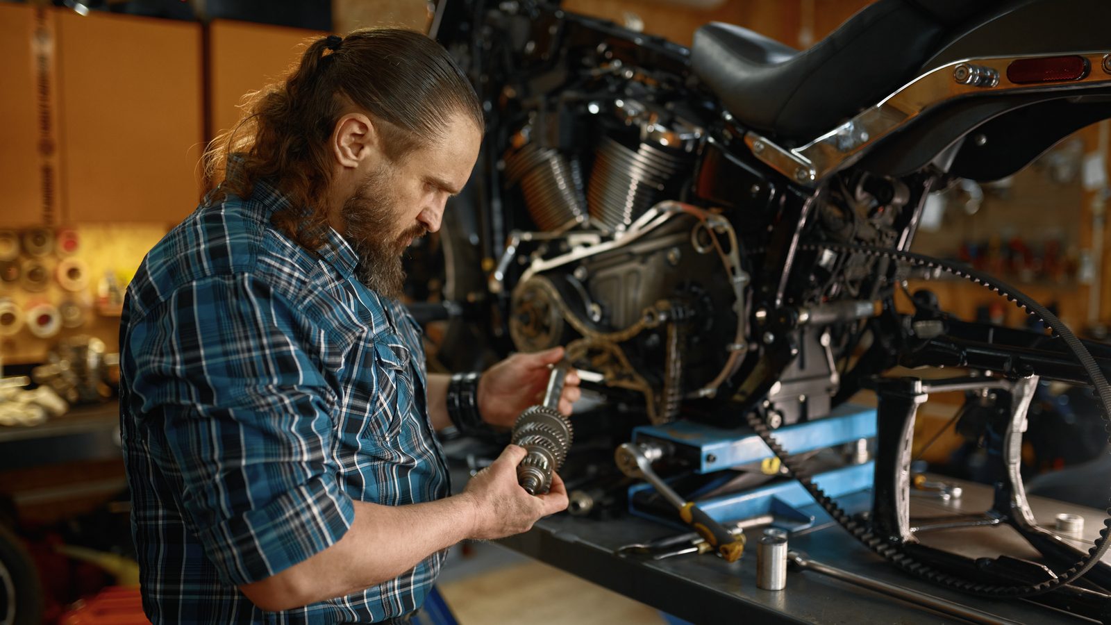 Mécanicien examinant une pièce moteur dans sa main, atelier de moto en arrière-plan
