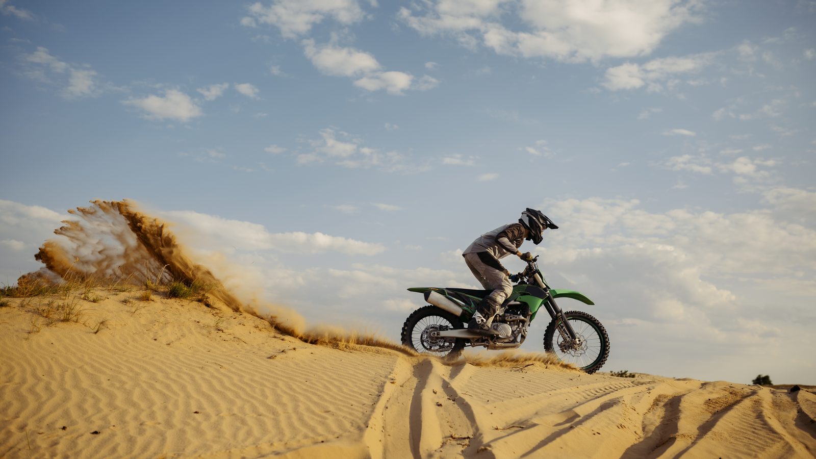 Moto tout-terrain descendant une pente de sable, pilote en retrait derrière la selle