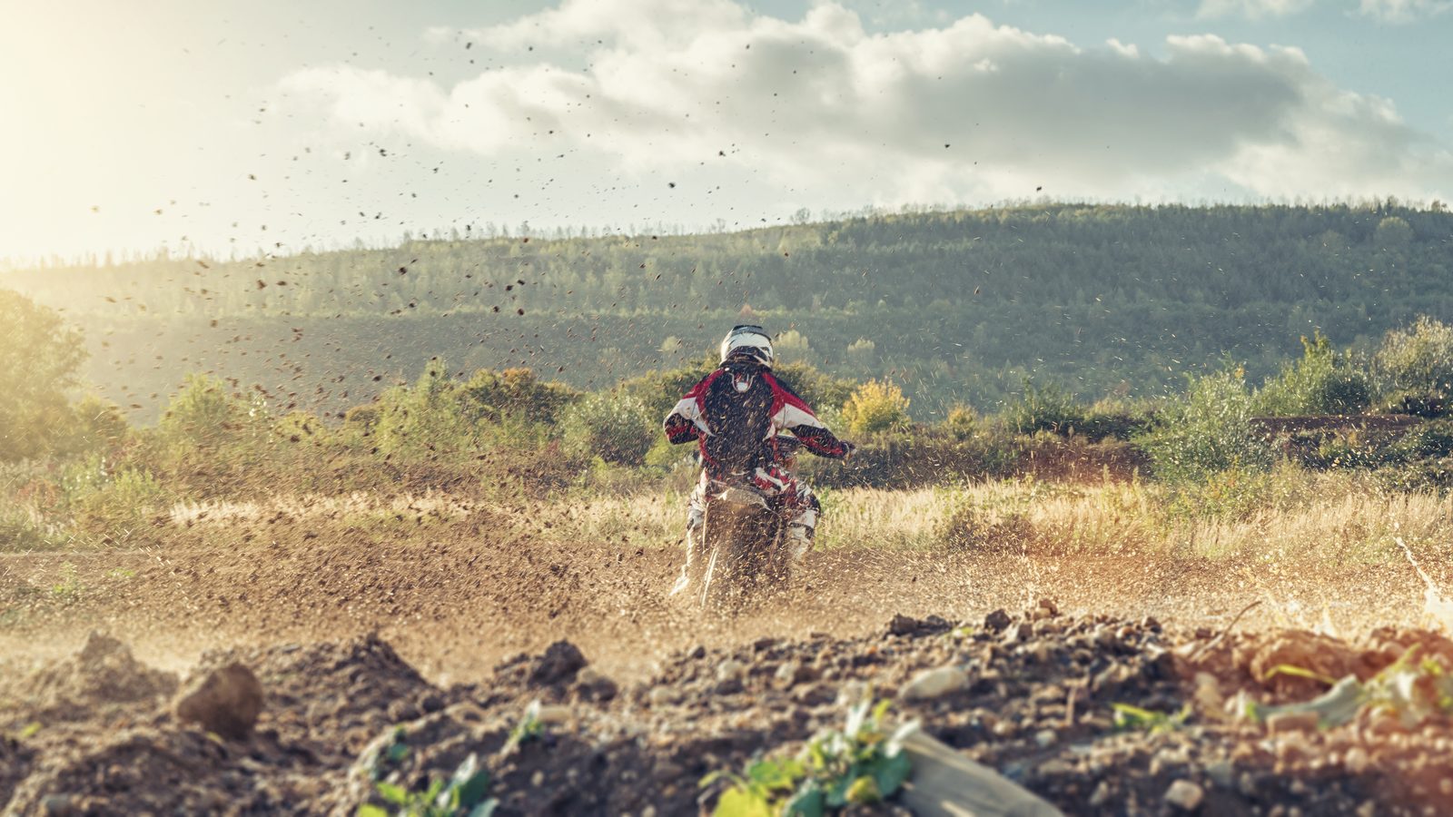 Moto tout-terrain roulant à allure modérée sur une piste de terre, paysage ouvert