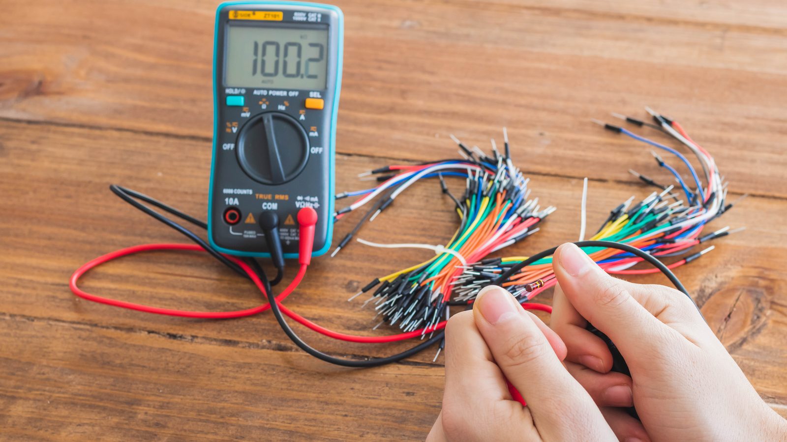 Multimètre numérique posé sur un établi, entouré de fils électriques de couleurs différentes