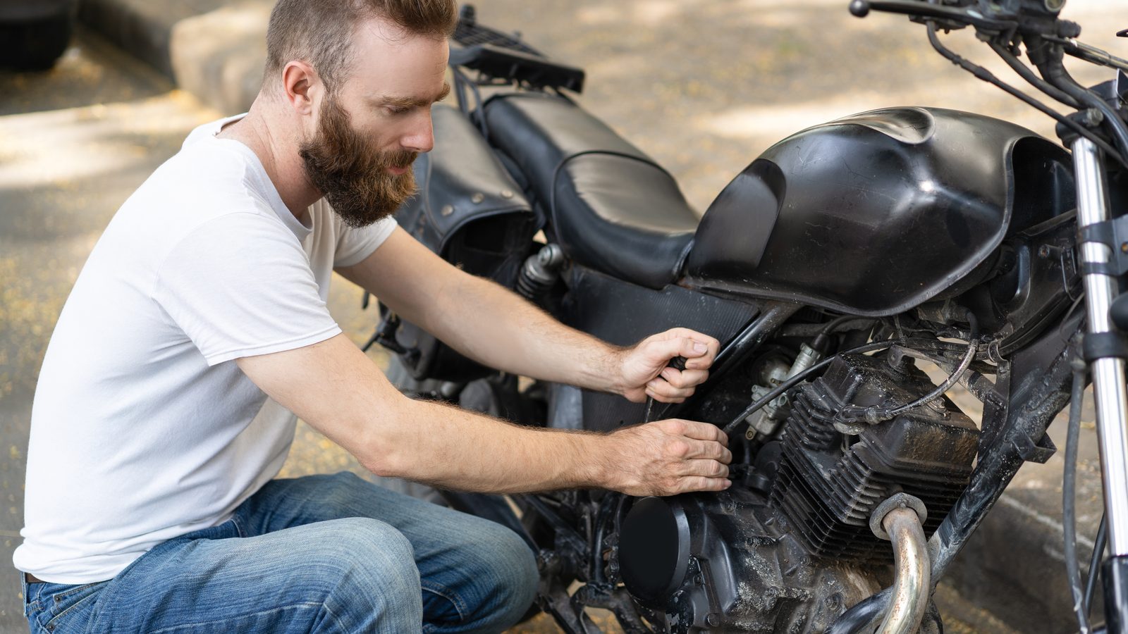 Pilote accroupi près de sa moto arrêtée en pleine nature, tentant de la faire redémarrer