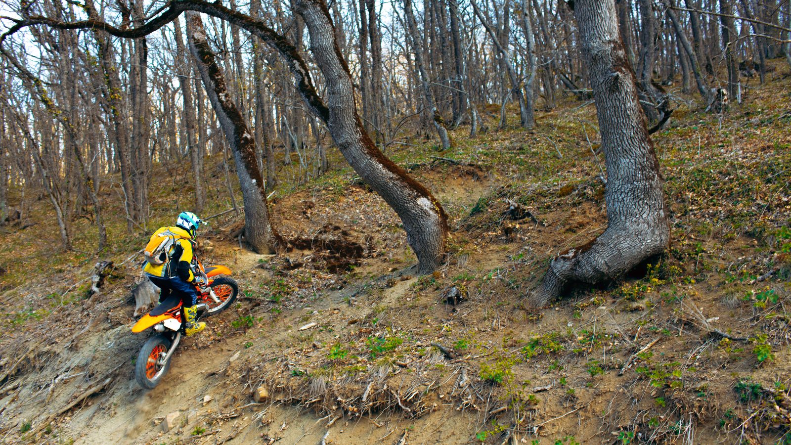 Pilote de moto tout-terrain gravissant une pente en terrain montagneux, corps porté vers l'avant