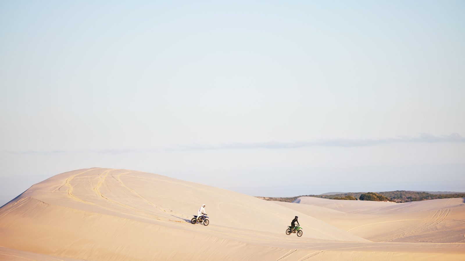 Pilote de moto tout-terrain lancé sur une étendue de sable, casque et tenue de protection