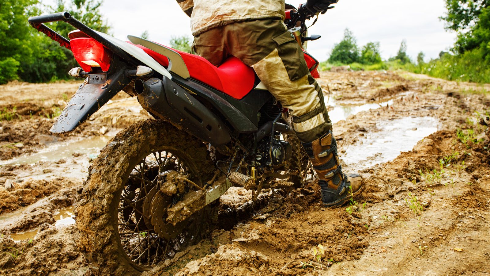 Pilote de motocross lancé dans une ornière détrempée, gerbe de boue projetée derrière la roue arrière
