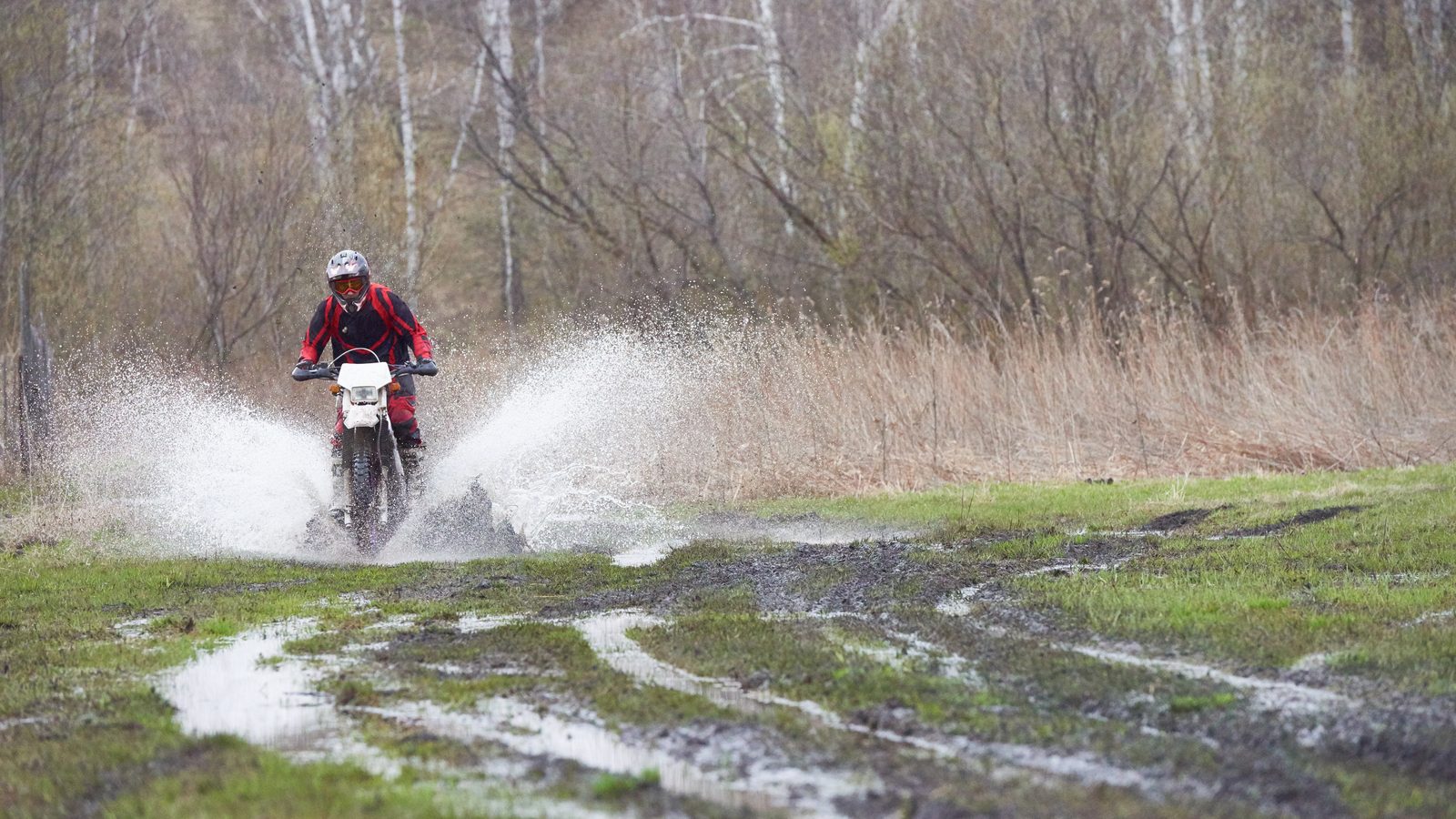 Pilote de motocross lancé sur une piste détrempée, projections de boue autour de la roue
