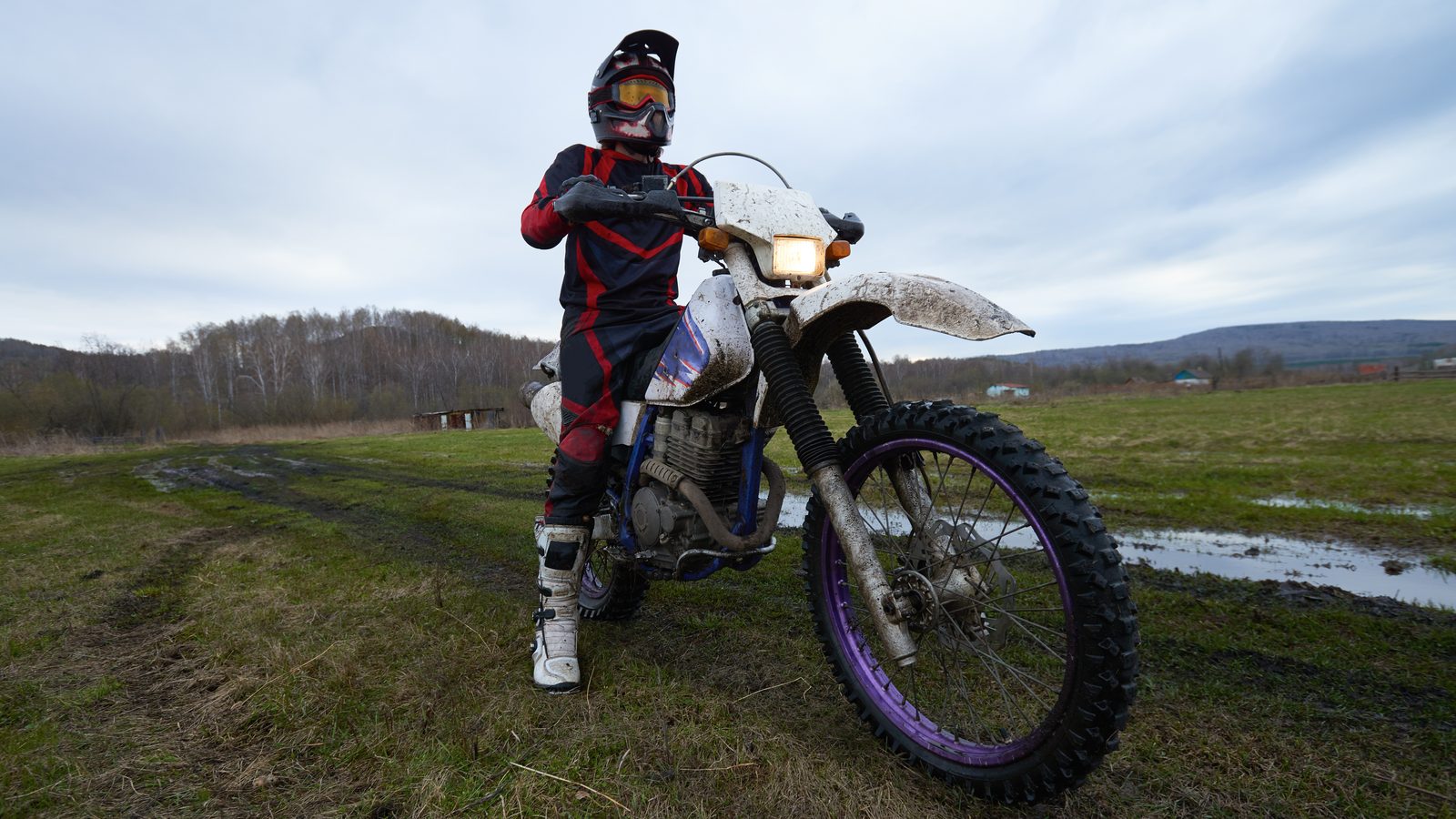 Pilote debout près de sa moto tout-terrain avant le départ, en bottes et tenue complète