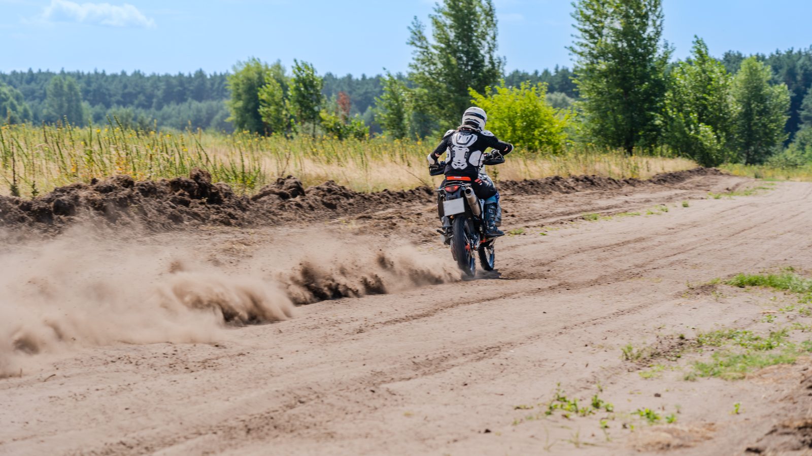 Piste de motocross poussiéreuse au relief marqué, pilote lancé sur une portion accidentée