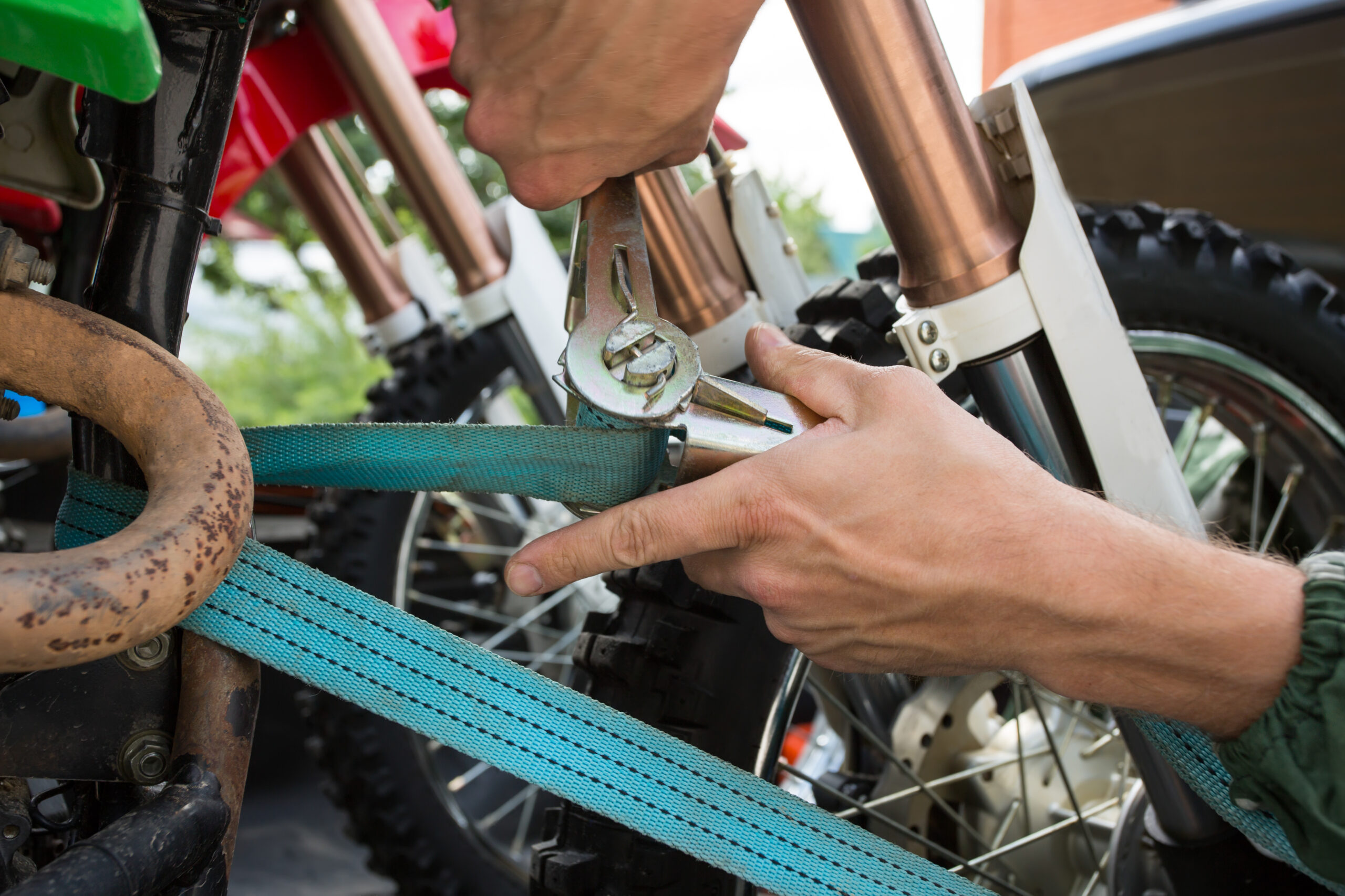 Main qui serre une sangle d'arrimage bleue pour fixer solidement une moto de motocross sur une remorque de transport.
