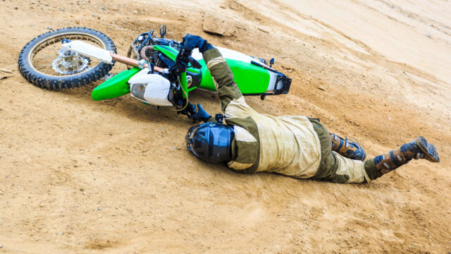 Pilote de moto en train de chuter, la moto couchée au sol pendant une glissade sur le terrain.