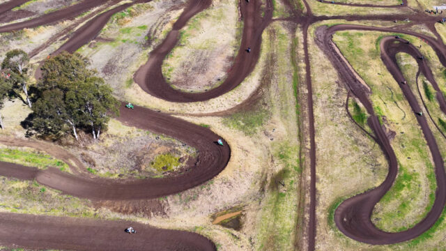 Vue aérienne d'une piste de motocross sinueuse en pleine campagne, avec des pilotes qui roulent sur le tracé en terre.