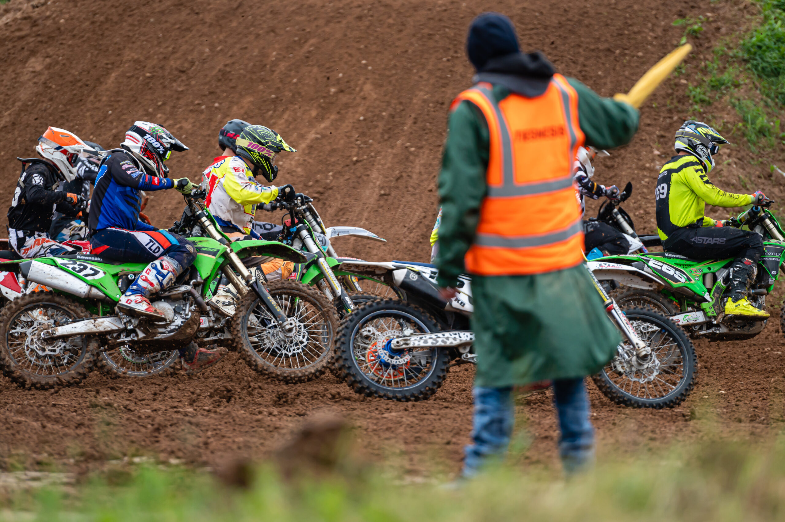 Groupe de pilotes de motocross roulant en peloton dans un virage sur un terrain vallonné et poussiéreux.