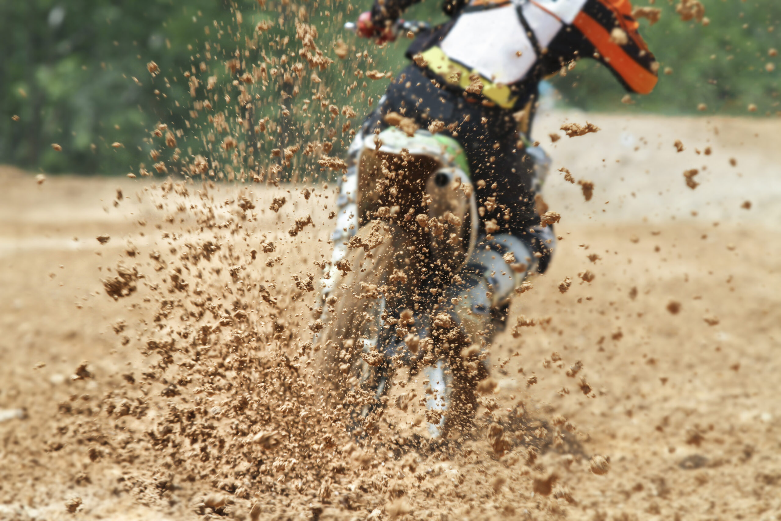 Pilote de motocross qui accélère fort, projetant une gerbe de terre derrière sa roue arrière sur la piste.