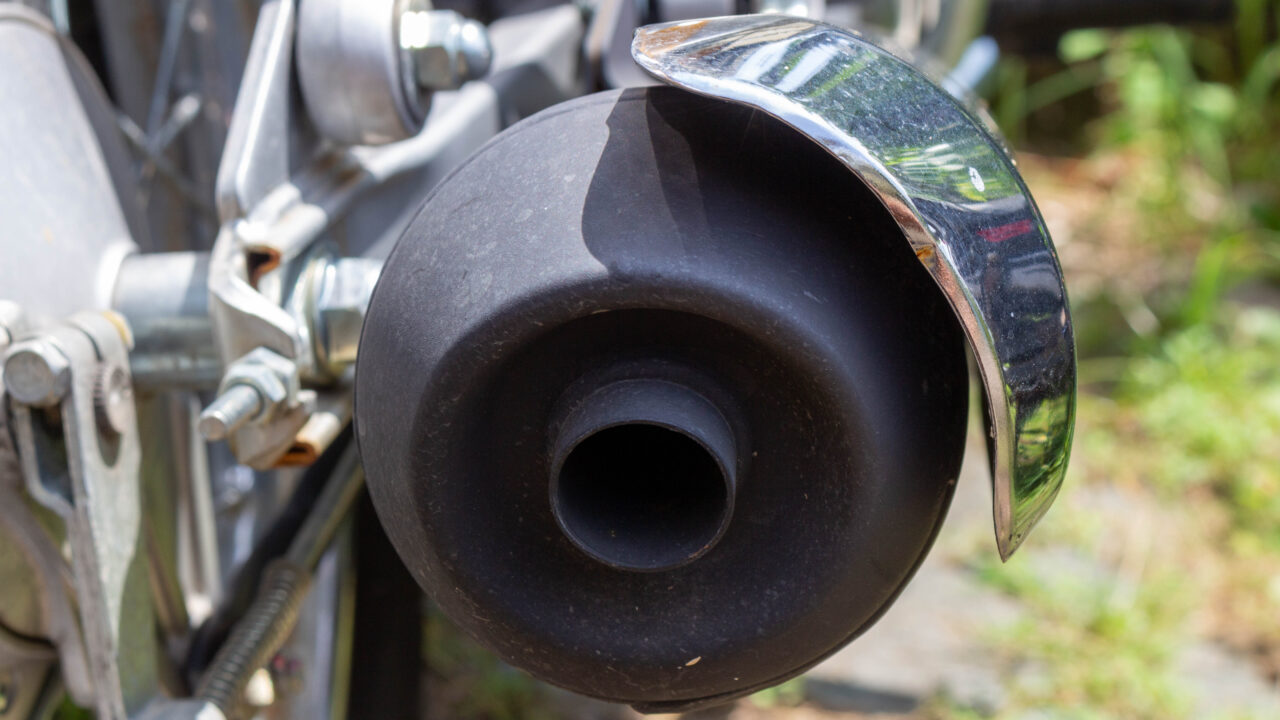 Gros plan sur l'échappement chromé d'une moto de motocross, symbole du bruit caractéristique du moteur.