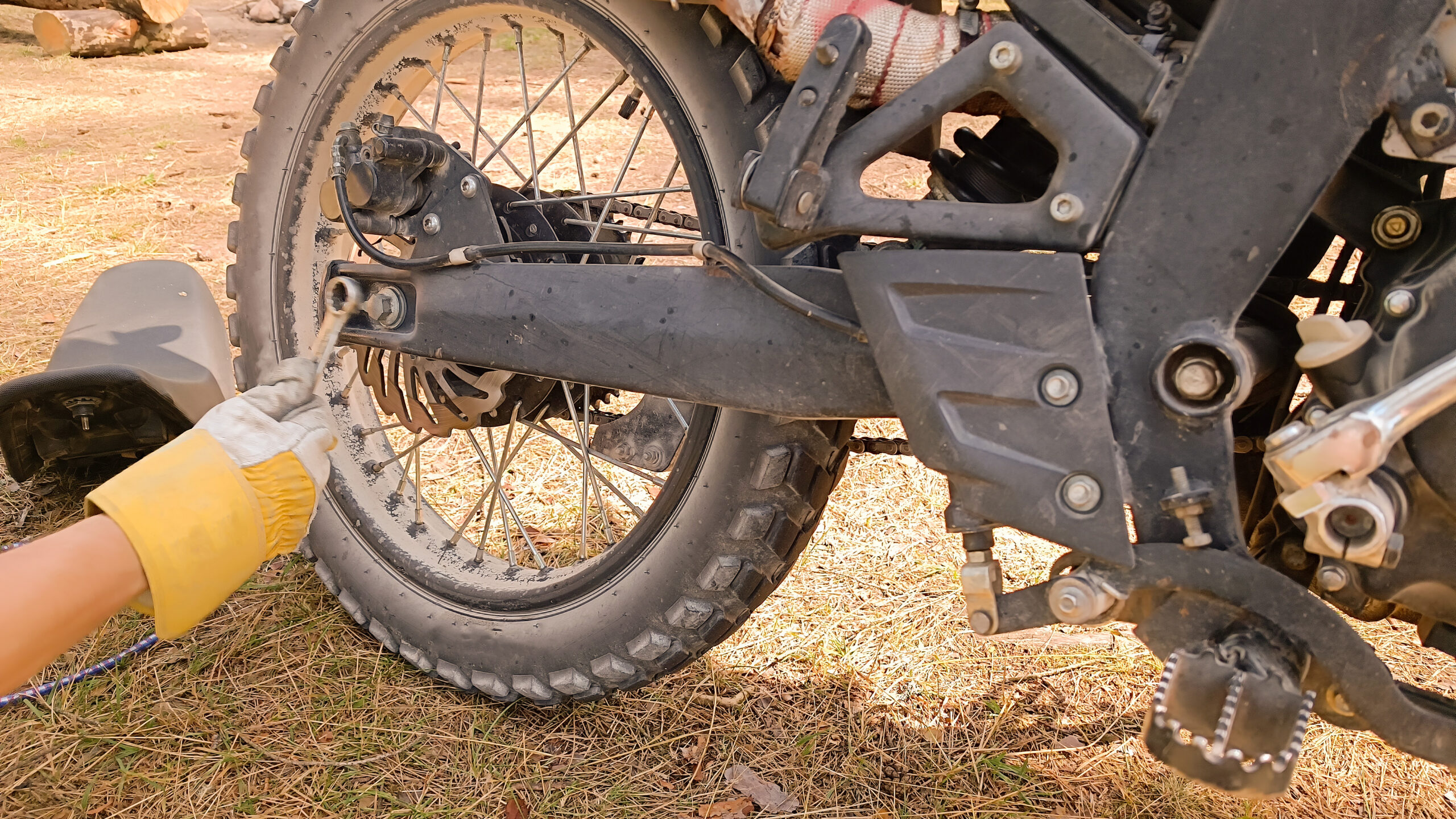 Gros plan sur une main gantée qui resserre un boulon sur la roue arrière d'une moto de motocross couverte de terre.