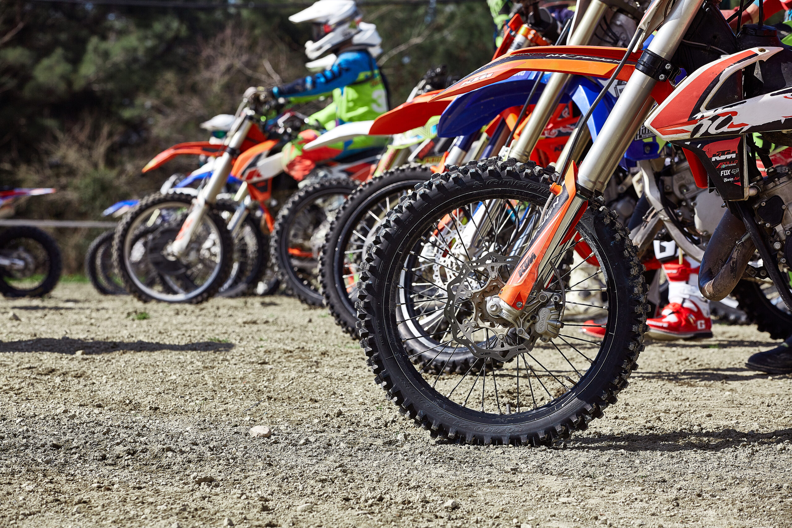 Jeunes pilotes de motocross alignés côte à côte sur leurs motos à la grille de départ, prêts à s'élancer pour la course.