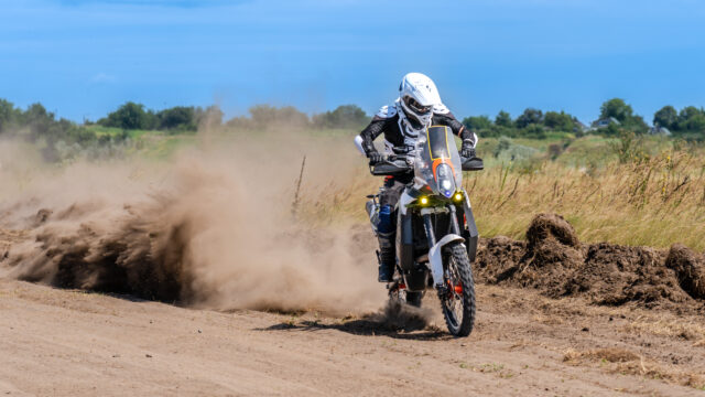Pilote de motocross roulant seul sur une piste poussiéreuse, moto penchée dans un virage avec un nuage de poussière derrière la roue.