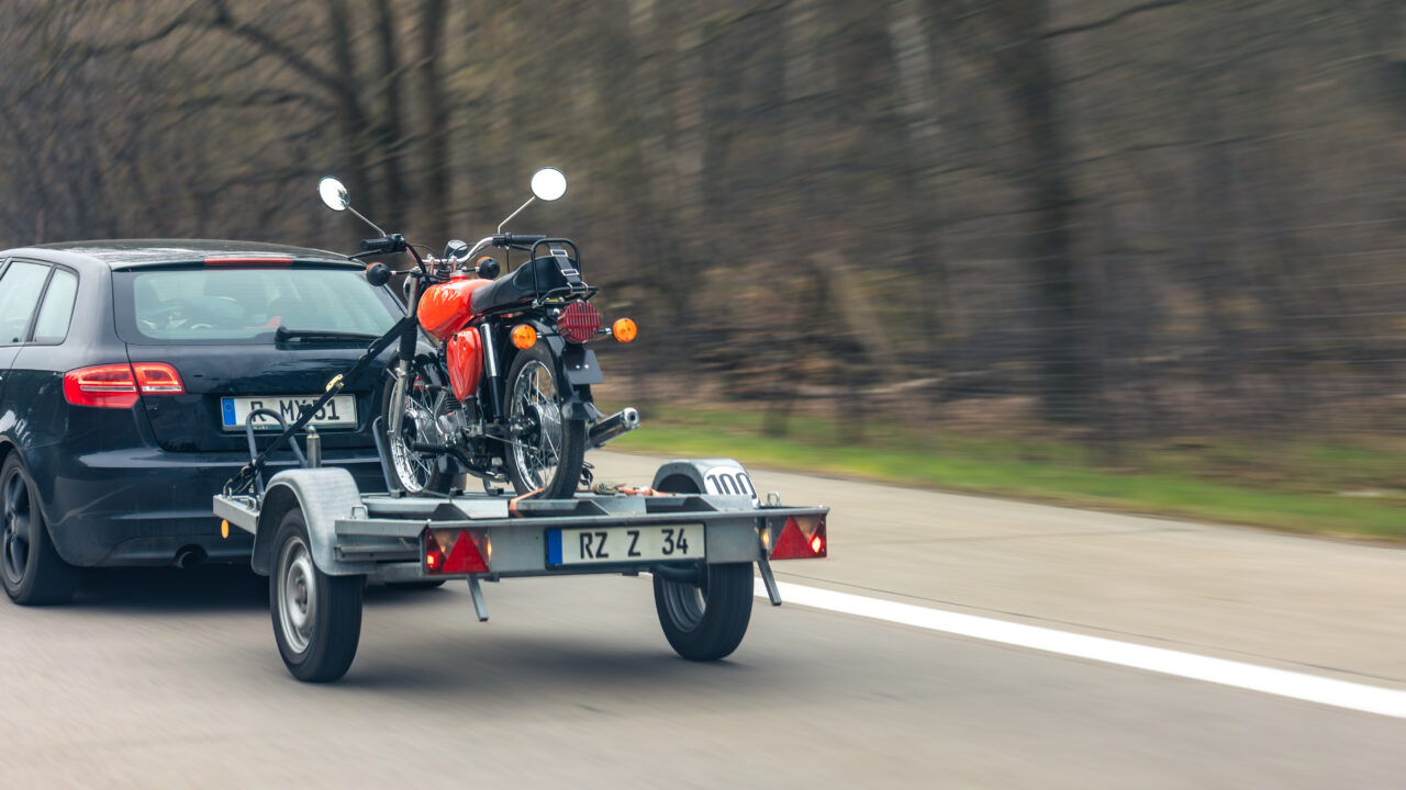 Voiture qui tracte une remorque chargée d'une moto sur l'autoroute pour l'emmener jusqu'au terrain de motocross.