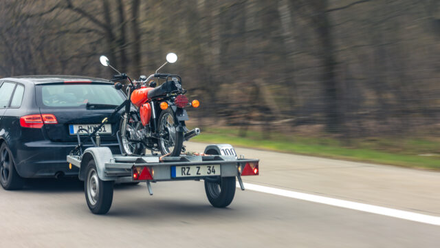 Voiture qui tracte une remorque chargée d'une moto sur l'autoroute pour l'emmener jusqu'au terrain de motocross.