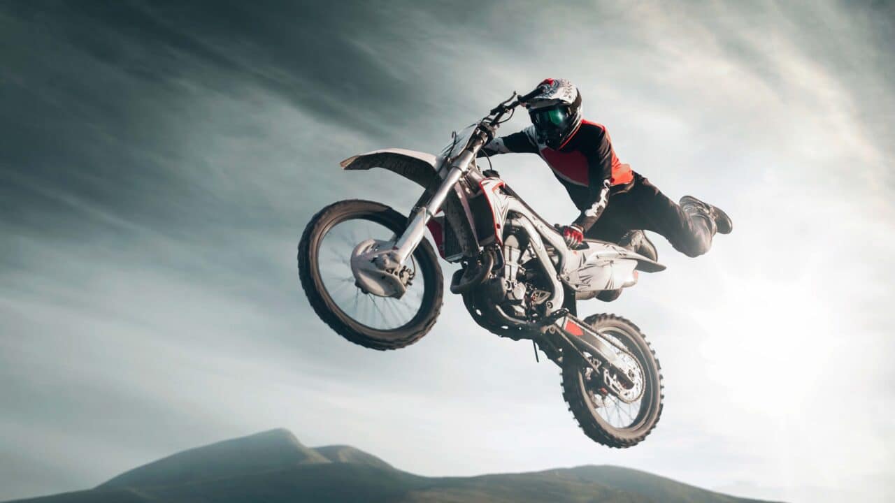 Pilote de motocross en plein saut, moto à l'horizontale sous un ciel clair et lumineux