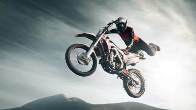 Pilote de motocross en plein saut, moto à l'horizontale sous un ciel clair et lumineux