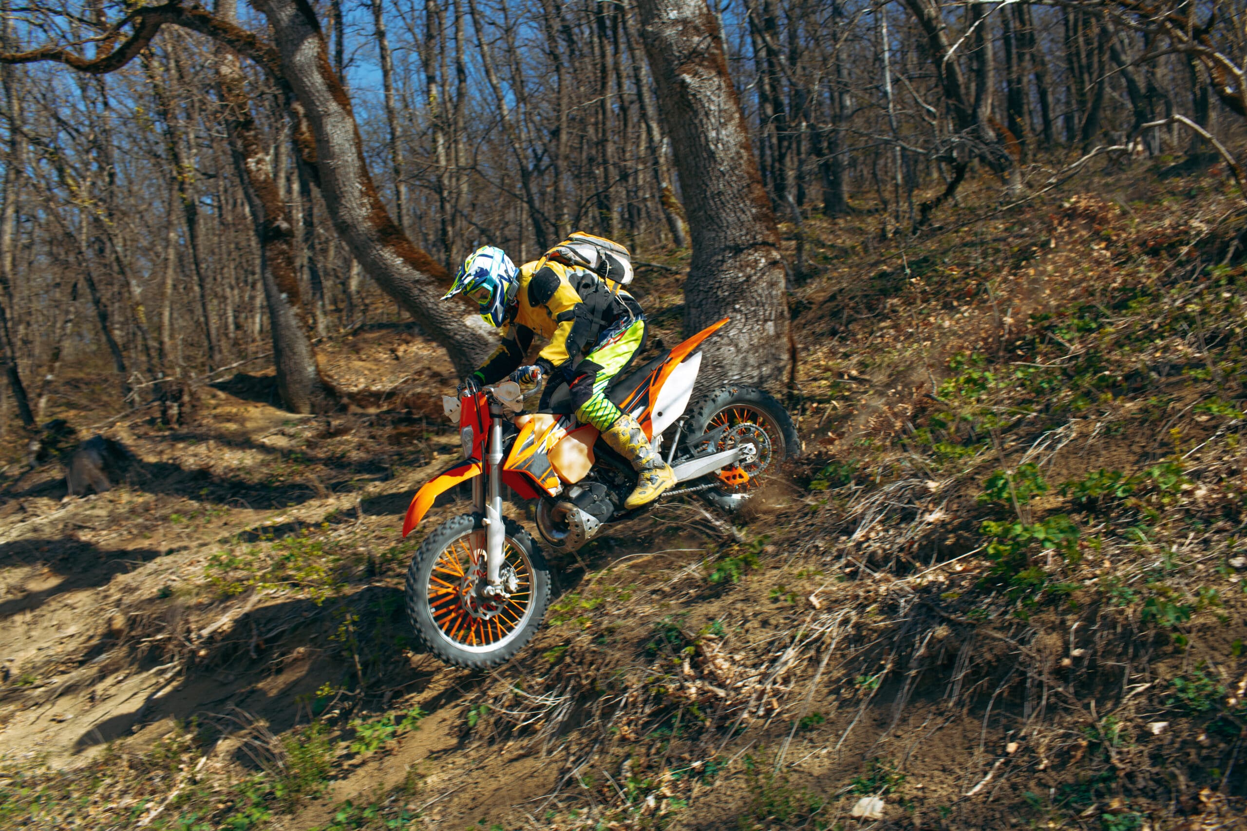 Pilote de motocross dévalant un chemin sec et poussiéreux en sous-bois, sous un soleil franc