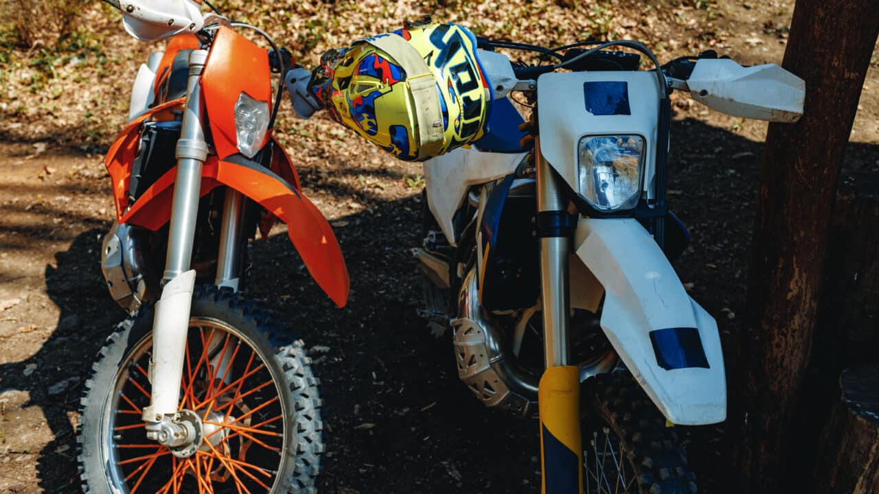 Deux motos de motocross garées phare contre phare, une orange et une blanche, dans une clairière en automne