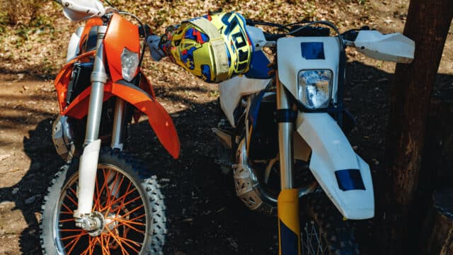 Deux motos de motocross garées phare contre phare, une orange et une blanche, dans une clairière en automne
